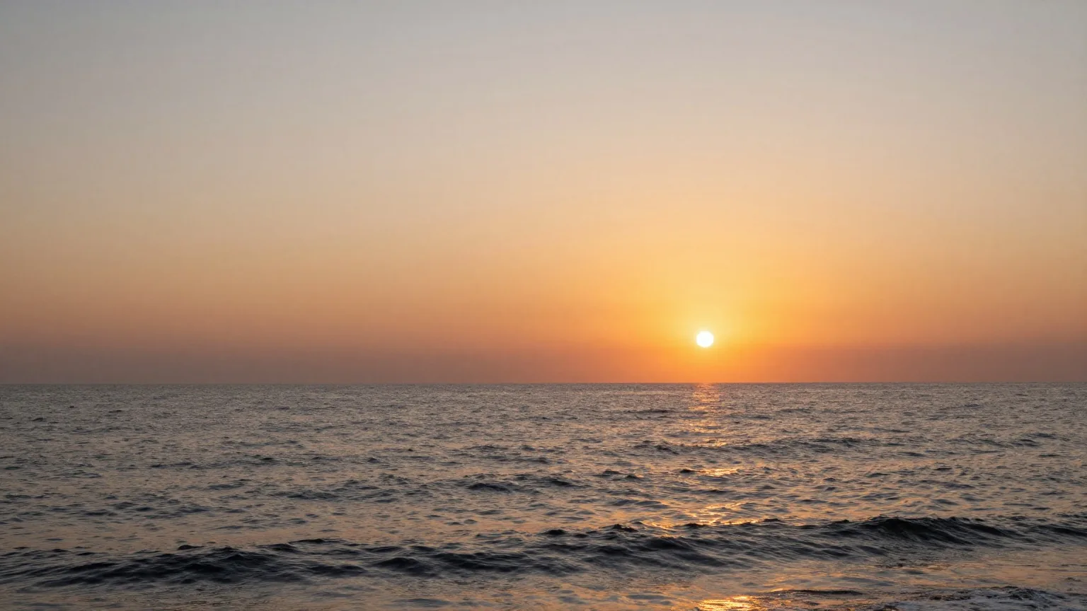 Orange leuchtender Abendhimmel über ruhigem Meer, die Sonne sinkt an einem wolkenlosen Westhorizont