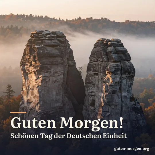 Sandsteinfelsen ragen bei Sonnenaufgang aus dem Morgennebel über einem Herbstwald, warmes Licht auf dem Gestein; Schrift: „Guten Morgen! Schönen Tag der Deutschen Einheit“