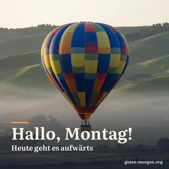 Bunter Heißluftballon steigt bei Tagesanbruch über grünen Hügeln auf, in den Tälern liegt Nebel; Schrift: „Hallo, Montag! Heute geht es aufwärts“