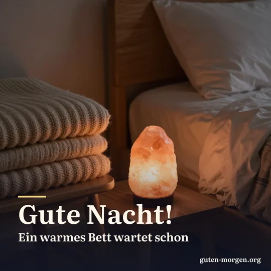 Warm leuchtende Salzkristalllampe neben einer gefalteten groben Wolldecke auf einem Holzstuhl am Bett, bernsteinfarbenes Licht im dunklen Schlafzimmer; Schrift: „Gute Nacht! Ein warmes Bett wartet schon“