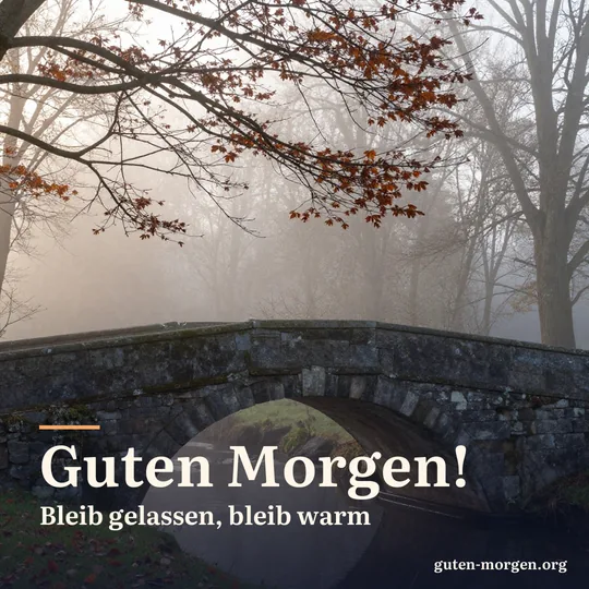 Alte Steinbrücke über einen nebligen Bach bei Sonnenaufgang, an den Zweigen hängt das letzte kupferfarbene Buchenlaub; Schrift: „Guten Morgen! Bleib gelassen, bleib warm“