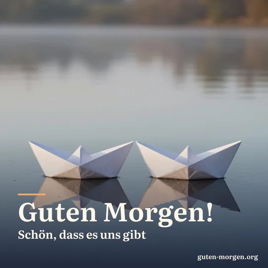 Zwei weiße Papierschiffchen schwimmen nebeneinander auf einem stillen Teich bei Sonnenaufgang, zarte Spiegelungen in Pastellfarben; Schrift: „Guten Morgen! Schön, dass es uns gibt“