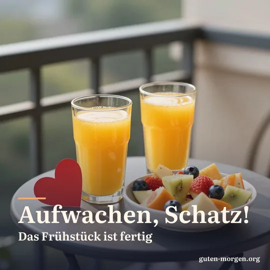Zwei Gläser frisch gepresster Orangensaft und eine Schale bunter Obstsalat auf einem Balkontisch in der Morgensonne, daneben ein kleines rotes Papierherz; Schrift: „Aufwachen, Schatz! Das Frühstück ist fertig“
